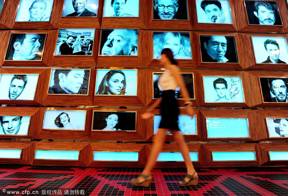 Una mujer camina junto a una pared de fotos de famosos en el cine "Amy 1895" de Shenyang, el 13 de agosto de 2014. [Foto/CFP]