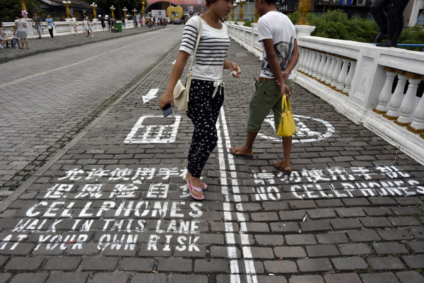 Personas caminan por una acera que se divide en dos vías: una para los que utilizan teléfonos celulares, y la otra para los que no lo usan. Chongqing.
