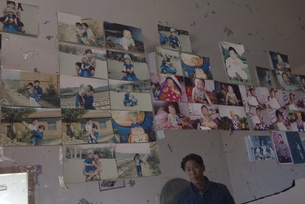 El padre de Pan Xiaomei se inclina contra la pared donde están las fotos de Pan y su hijo. [Foto: PPC]