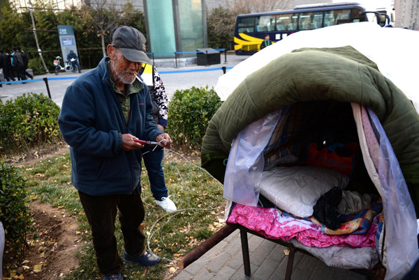 Un anciano descansa junto a su carreta de fabricación casera en la avenida Chang'an de Pekín, el 21 de noviembre. [Foto/IC]