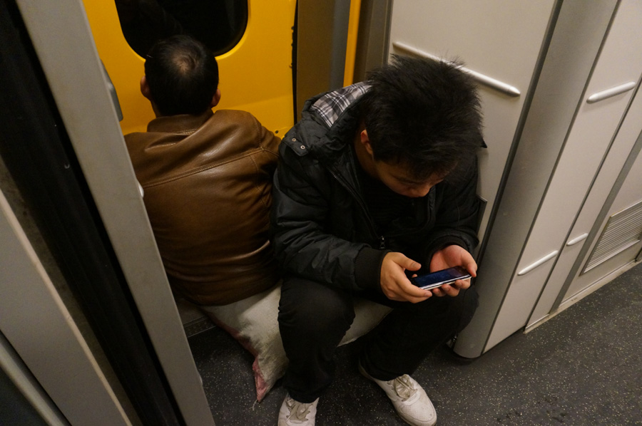 Dos pasajeros que compraron billetes para ir de pie se sientan sobre sus equipajes. [Fotografía de Zhang Xiang/chinadaily.com.cn]