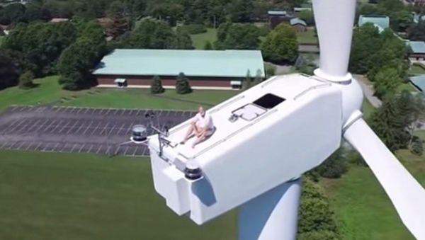 Un dron graba a un hombre tomando el sol sobre un aerogenerador eólico