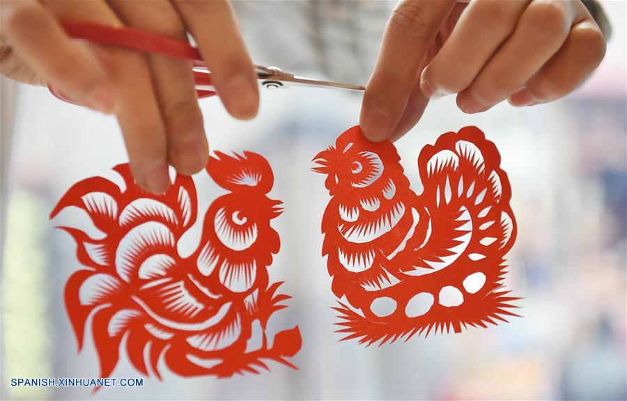 Imagen del 29 de diciembre de 2016 de Chang Yangyang, un joven artista folclórico, mostrando sus trabajos de papel cortado de un gallo y una gallina, en el condado de Mengjin, provincia de Henan, en el centro de China. Los chinos celebrarán el Año Nuevo Lunar, o Festival de Primavera, el 28 de enero de 2017. El Festival de Primavera esta vez marca el comienzo del Año del Gallo, de acuerdo con el zodíaco chino que asigna uno de los 12 animales a cada año. (Xinhua/Huang Zhengwei)