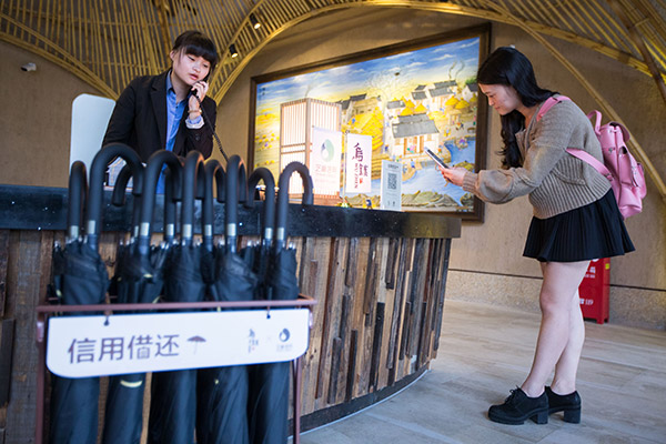 Un turista toma utiliza un paraguas compartido del sistema Créditos Zhima en Wuzhen, provincia de Zhejiang. [Foto: proporcionada]