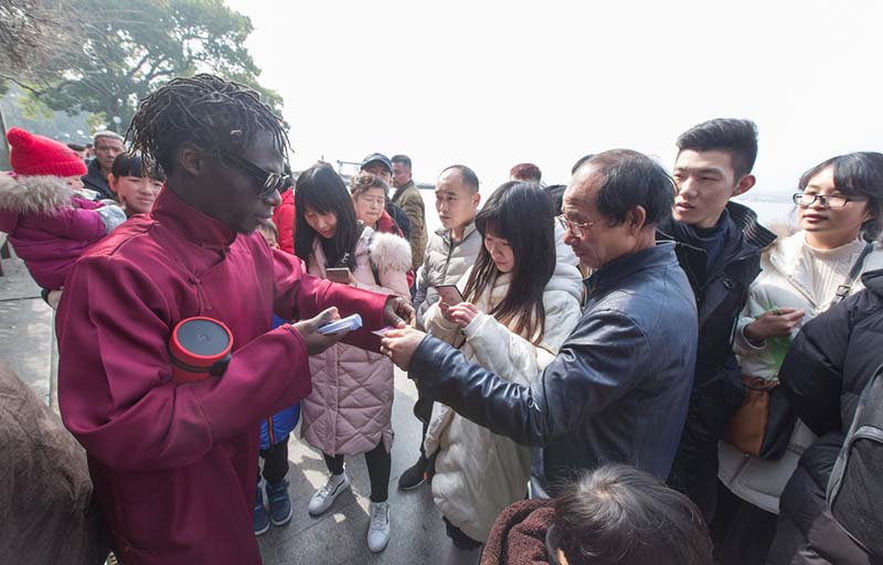 El hombre de rojo tiene el nombre chino de Xing Fu, que significa felicidad. Viene de Nigeria y a menudo practica recitando poemas tradicionales chinos cerca en el Lago Oeste de Hangzhou, provincia de Zhejiang. Él reparte sus tarjetas a los transeúntes el 2 de febrero de 2018. [Foto / IC]