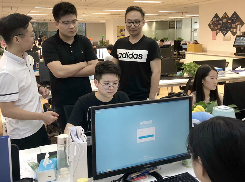Zheng Wencheng (segundo a la izquierda, con los brazos cruzados), fundador y presidente ejecutivo de Hyphen, supervisa el desarrollo de software en la división de investigación y desarrollo de la empresa. [Foto proporcionada a China Daily]