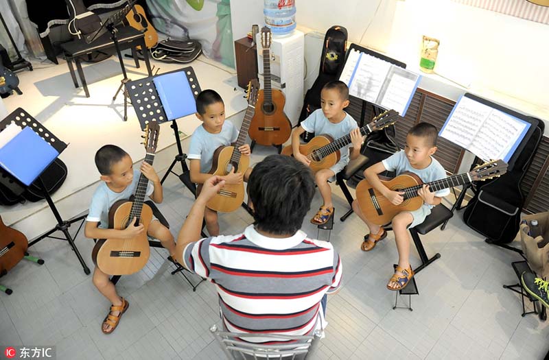 Los cuatrillizos tocan la guitarra en Jinan, provincia de Shandong, 2 de agosto del 2018. [Foto: IC]