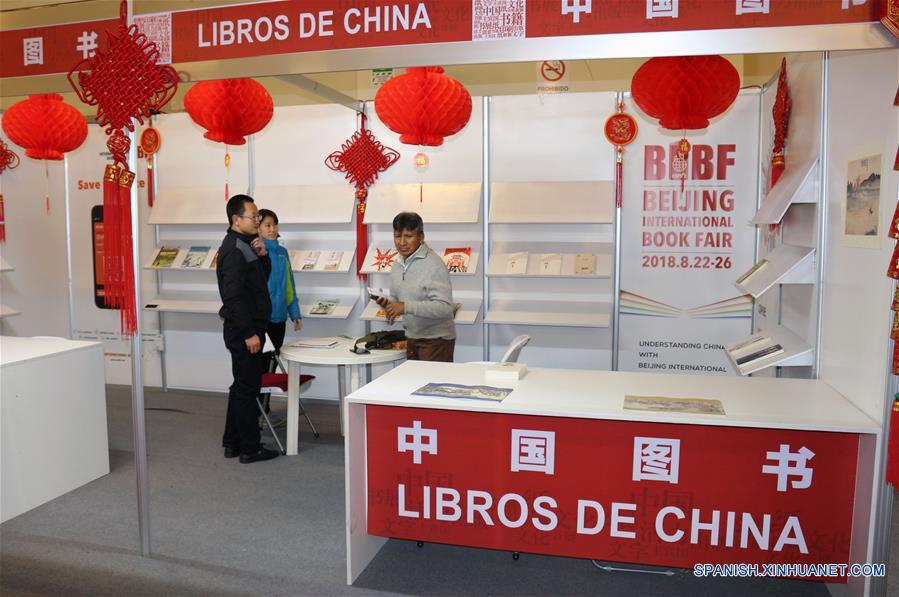 Imagen del 9 de agosto de 2018 de los encargados del estand de China, Li Ruixia (i-atrás) y Lu Shuming (i-frente) conversando con una persona en el estand "Pabellón Rojo" de la Feria Internacional del Libro (FIL) de La Paz 2018, en La Paz, Bolivia. En el "Pabellón Rojo" de la Feria Internacional del Libro (FIL) de La Paz 2018 se instala un puesto, donde China, con la distinción de "Invitado Destacado", ocupa un lugar sobresaliente en la exposición que inició el pasado 1 de agosto y se extenderá hasta el domingo 12 de agosto. (Xinhua/René Quenallata)