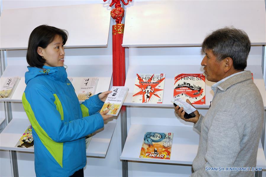 Imagen del 9 de agosto de 2018 de Li Ruixia (i), mostrando un libro a una persona en el estand "Pabellón Rojo" de la Feria Internacional del Libro (FIL) de La Paz 2018, en La Paz, Bolivia. En el "Pabellón Rojo" de la Feria Internacional del Libro (FIL) de La Paz 2018 se instala un puesto, donde China, con la distinción de "Invitado Destacado", ocupa un lugar sobresaliente en la exposición que inició el pasado 1 de agosto y se extenderá hasta el domingo 12 de agosto. (Xinhua/René Quenallata)