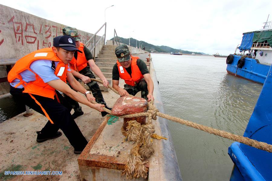Guardias fronterizos y policías locales ayudan a amarrar botes pesqueros en un muelle, en el distrito Luqiao de la ciudad de Taizhou, provincia de Zhejiang, en el este de China, el 12 de agosto de 2018. El Centro Meteorológico Nacional (CMN) de China elevó el domingo el nivel de alerta por el tifón Yagi de azul a amarillo, el tercero más alto, a la espera de que toque tierra esta noche en la región costera oriental del país. (Xinhua/Jiang Youqin)