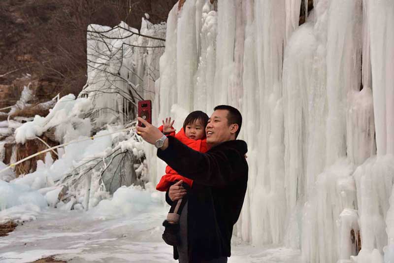 Un hombre se toma una foto junto a un niño en la montaña Wuzhishan de Handan, provincia de Hebei, 15 de enero del 2019. [Foto: Yang Yanzhong/ Chinadaily.com.cn]