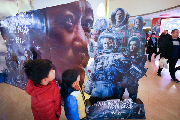 Los espectadores miran un póster que promociona el éxito en taquilla de ciencia ficción The Wandering Earth el domingo en Beijing. [FOTO POR ZHU XINGXIN / CHINA DAILY]
