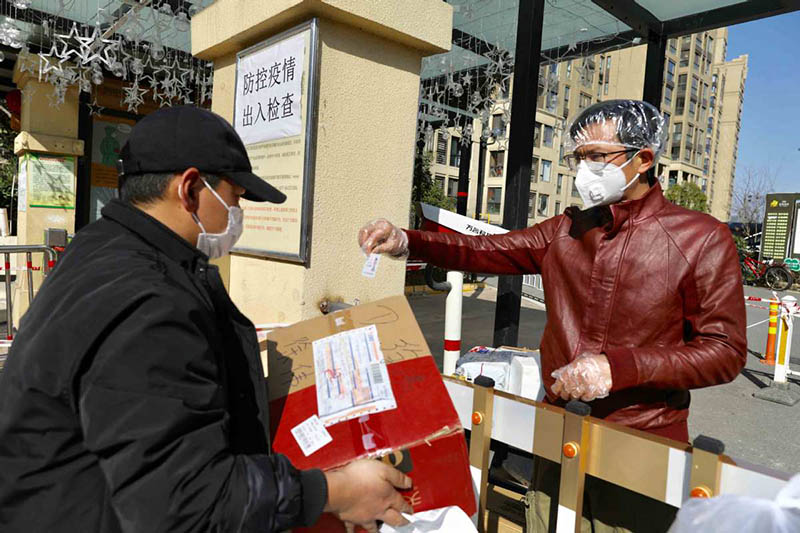 Un hombre busca su compra en la puerta de una comunidad residencial en Wuhan, provincia de Hubei, 18 de febrero del 2020. [Foto: Zhu Xingxin / China Daily]