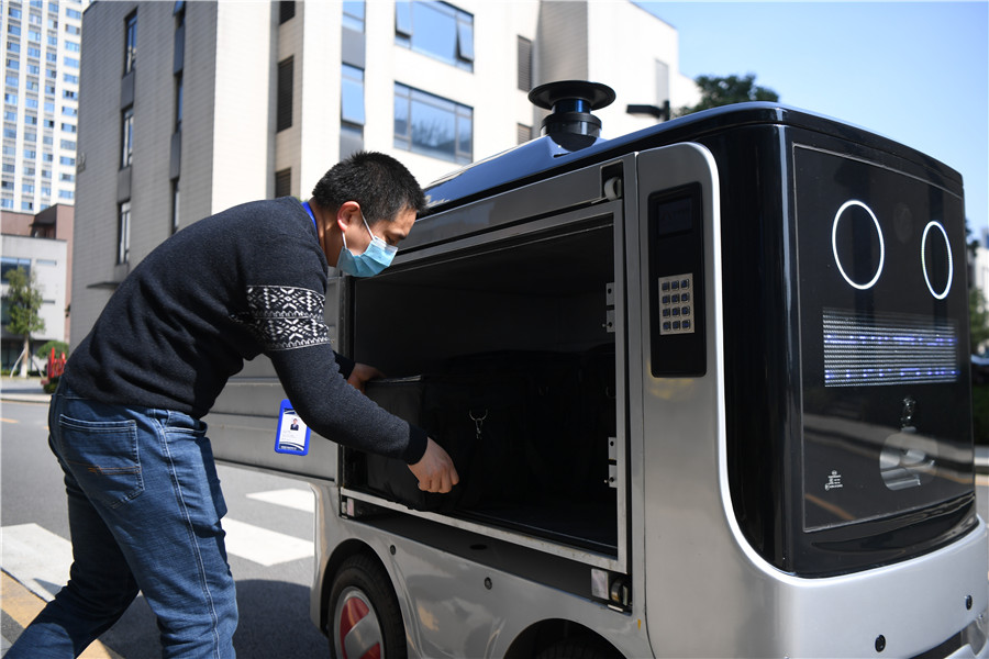 Un empleado de un puerto de fabricación inteligente busca su caja de comida en un vehículo robot de reparto en Changsha, provincia de Hunan, 14 de febrero del 2020. [Foto: Xinhua]
