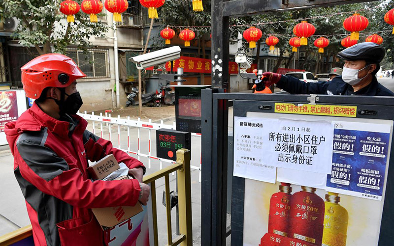 Un repartidor de JD (a la izquierda) espera que le controlen la temperatura en la puerta de una comunidad residencial que ha instalado un armario especial para depositar paquetes en Xi'an, capital de la provincia de Shaanxi, 3 de febrero del 2020. [Foto: Xinhua] 