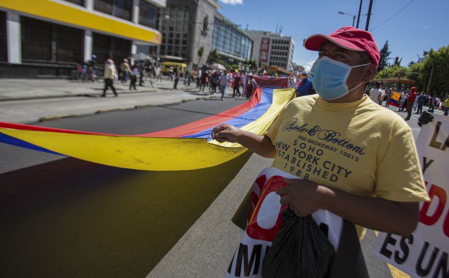 Un manifestante porta una mascarilla mientras sostiene una bandera ecuatoriana durante una marcha en contra de las medidas adoptadas por el gobierno debido a la enfermedad causada por el nuevo coronavirus (COVID-19), una de las cuales es la reducción de dos horas diarias la jornada laboral, en Quito, Ecuador, el 25 de mayo de 2020. (Xinhua/Santiago Armas)