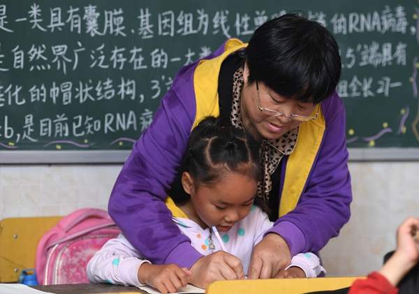 Una maestra ayuda a una alumna a escribir. [Foto / Xinhua]