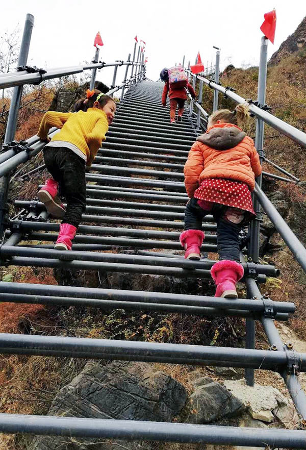 Los niños están subiendo las escaleras de acero de la "aldea del acantilado" bajo la guía de los padres en un proyecto de turismo cultural en enero de 2018. Esta actividad no solo puede garantizar la seguridad, sino también aumentar el coraje de los niños. (Foto: Rao Guojun/ Pueblo en Línea)