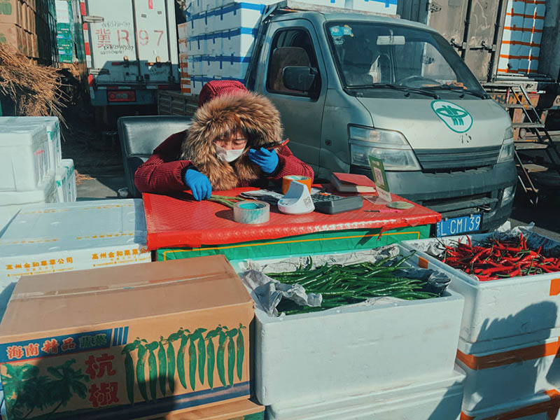 Wang Lijun, una vendedora de 43 años que lleva trabajando en el mercado Xinfadi desde hace más de 15 años, regatea con su socio por teléfono móvil. (Pueblo en Línea / Kou Jie)