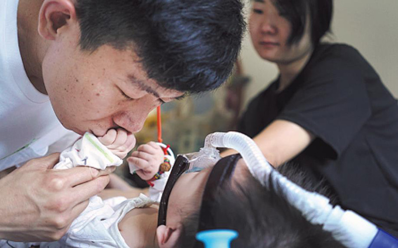 Un padre en Xiamen, provincia de Fujian, besa a su hija, que padece AME. [Foto: Liu Tao/ China Daily]