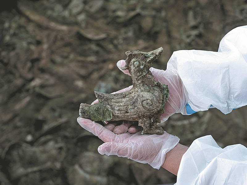 Un investigador extrae una estatuilla de bronce en forma de pájaro de un pozo de sacrificio en las ruinas de Sanxingdui, Guanghan, provincia de Sichuan, 9 de febrero del 2022. [Foto: Yu Jia/ China Daily]