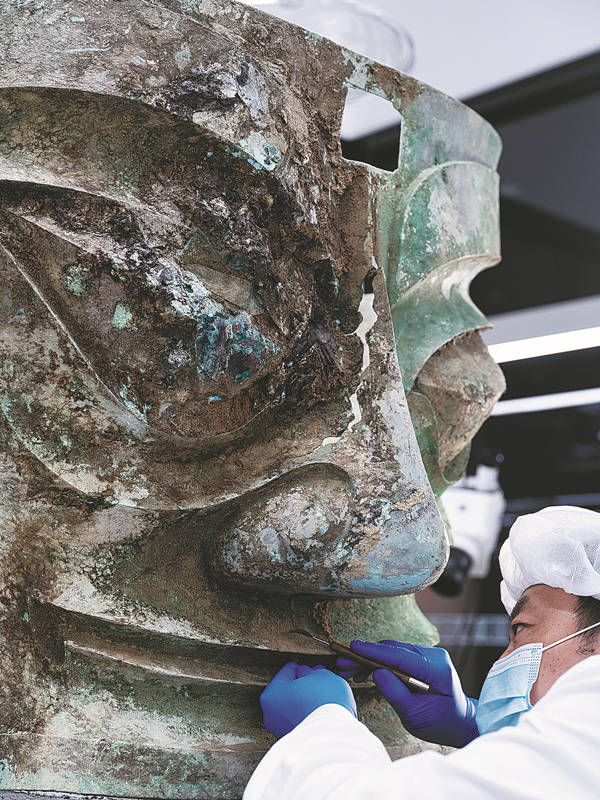 Un arqueólogo limpia la superficie de una máscara de bronce en las ruinas de Sanxingdui, Guanghan, provincia de Sichuan. [Foto: Yu Jia/ China Daily]
