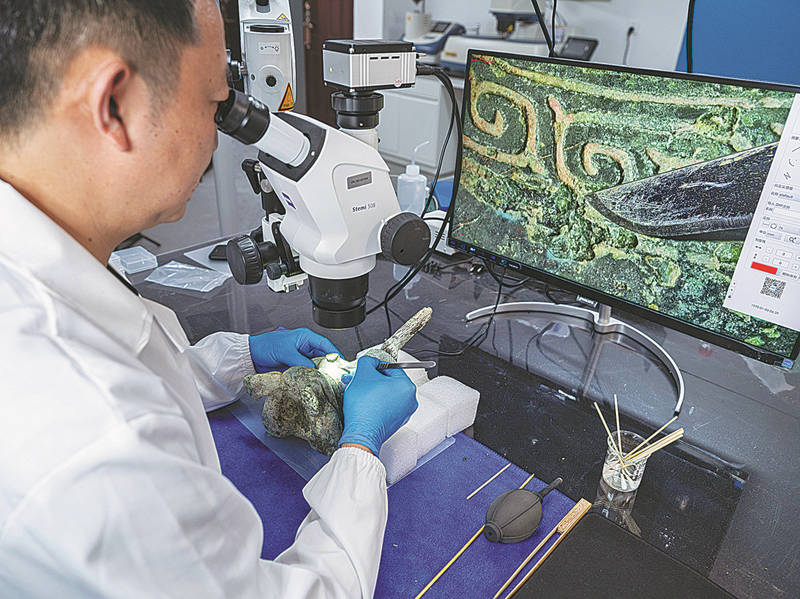 Un investigador utiliza un microscopio para reparar una estatuilla de bronce en un laboratorio del sitio de excavación en Sanxingdui, Guanghan, provincia de Sichuan, 9 de junio del 2022. [Foto: Yu Jia/ China Daily]