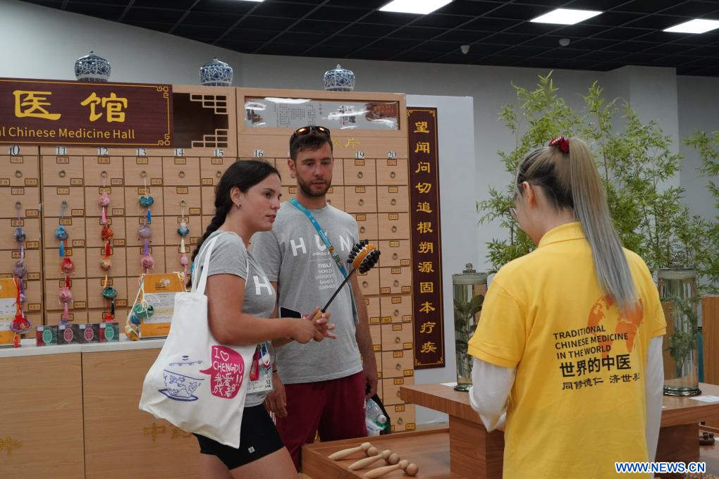 Imagen del 2 de agosto de 2023 de la atleta húngara, Anna Poltz (i) y su compañero de equipo aprendiendo sobre una herramienta de cuidado de la salud de medicina tradicional china (MTC) en la Aldea de los Juegos de la FISU, en Chengdu, en la provincia de Sichuan, en el suroeste de China. (Xinhua/Tang Wenhao)