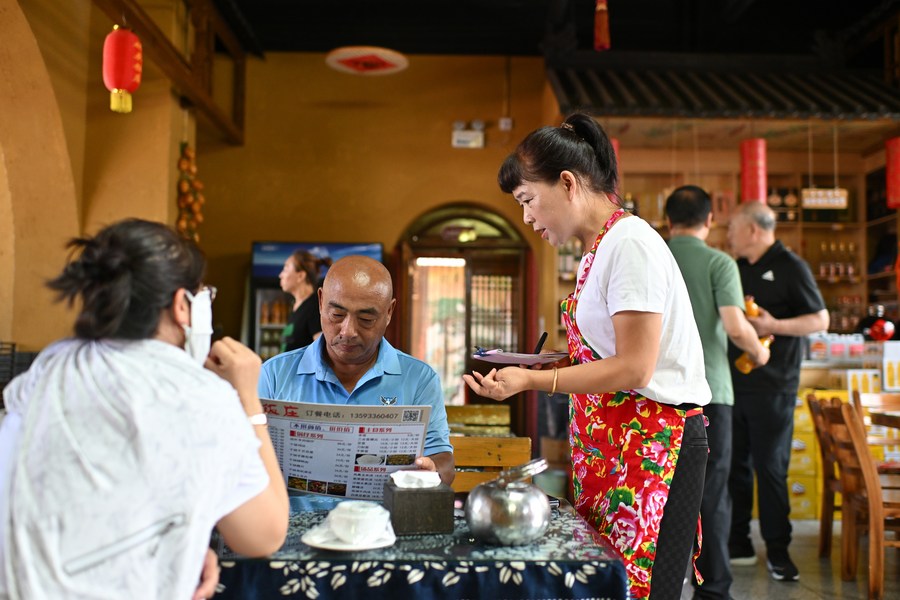 Jia Juan (derecha) presenta los platos de su propio restaurante a los turistas que visitan el poblado antiguo de Qikou del distrito de Linxian, en la provincia septentrional china de Shanxi, el 2 de agosto de 2023. (Xinhua/Zhan Yan)