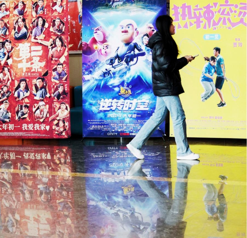 Una mujer camina frente a carteles de promoción de películas en un cine localizado en el distrito de Tancheng de la ciudad de Linyi, provincia de Shandong, en el este de China, el 15 de febrero de 2024. (Xinhua/Zhang Chunlei)