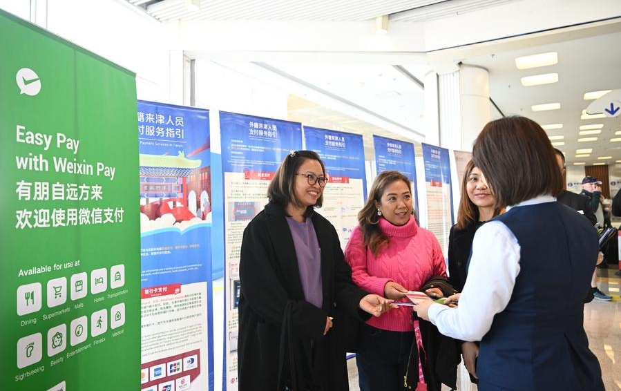 Una empleada proporciona materiales de guía sobre diferentes métodos de pago a turistas extranjeras, en la municipalidad septentrional china de Tianjin, el 7 de abril de 2024. (Xinhua/Sun Fanyue)