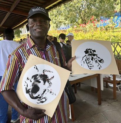  Emile Gankama, miembro del grupo conjunto de entrevistas e investigación del Foro de Cooperación de los Medios de Comunicación de la Franja y la Ruta 2024, muestra un cuadro pintado en cooperación. (Foto de Xu Hangyan, Diario del Pueblo)