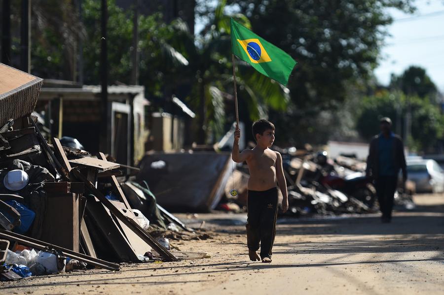 Un niño sostiene una bandera nacional brasileña mientras camina por una calle afectada por las inundaciones provocadas por las fuertes lluvias, en la Isla Pintada, en la ciudad de Porto Alegre, capital del estado de Rio Grande do Sul, Brasil, el 18 de junio de 2024. (Xinhua/Lucio Tavora)