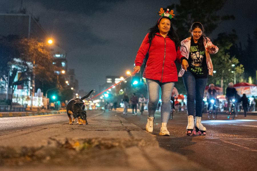 Imagen del 12 de diciembre de 2024 de mujeres caminando con su perro por una calle durante la Ciclovía Nocturna, en la ciudad de Bogotá, Colombia. (Xinhua/Andrés Moreno)