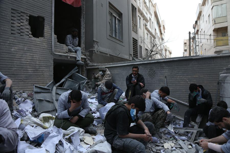 Imagen del 15 de marzo de 2026 de personas sentadas en los escombros de edificios destruidos en un área residencial, en Teherán, Irán. (Xinhua/Shadati)