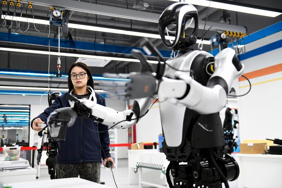 Una instructora supervisa el entrenamiento de un robot humanoide en un escenario de limpieza doméstica en un centro de capacitación de datos para inteligencia artificial incorporada, ubicado en el distrito de Pingyin, en la provincia oriental china de Shandong, el 21 de abril de 2026. (Xinhua/Guo Xulei)
