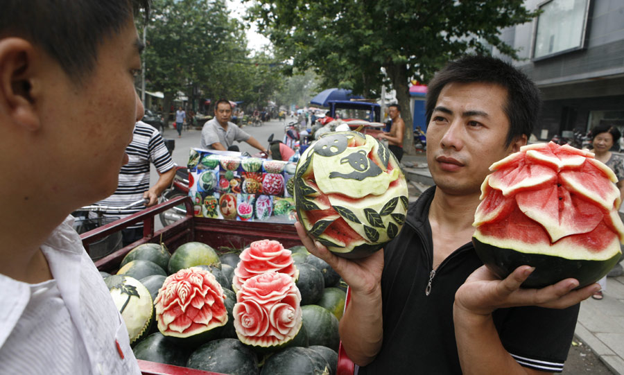 Zhang Yunxiao, un comerciante de frutas de 30 años de edad, trata de vender “sandías artísticas” a un cliente en Xiangyang, provincia de Hubei, el lunes 23 de julio de 2013. Zhang talla las sandías con formas de flores, como peonías y rosas, entre otras cosas. El precio de cada melón es de 20 yuanes (3,26 dólares) a 50 yuanes. (Foto: China Daily)