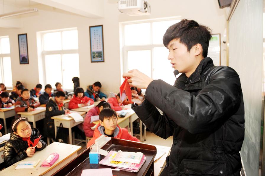 Chang Yangyang (derecha) da una lección de cortar papel en una escuela primaria de la ciudad de Mengjin, en Luoyang, provincia de Henan, el 2 de enero de 2014. Chang Yangyang, de 23 años, un artista y maestro del arte de cortar papel, dijo que el sueño de su vida era poder abrir un museo relacionado con el arte de cortar papel para que la gente pueda aprender más sobre este tesoro.