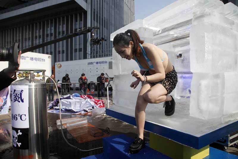 Una voluntaria intenta entrar en el cubo de hielo pero no soporta el frío y sale inmediatamente, en Changsha, provincia de Hunan, el 21 de enero de 2014. [Foto de Fu Zhiyong / Asianewsphoto]