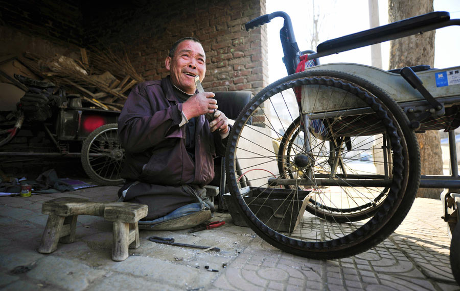 Lu Jianxin, quien perdió ambas extremidades en un incendio hace 30 años, arregla una silla de ruedas en Luoyang, provincia de Henan, el 16 de marzo, en un taller de reparación de bicicletas que ha dirigido desde hace más de dos décadas. [Fotografía por Huang Zhengwei/Asianewsphoto]