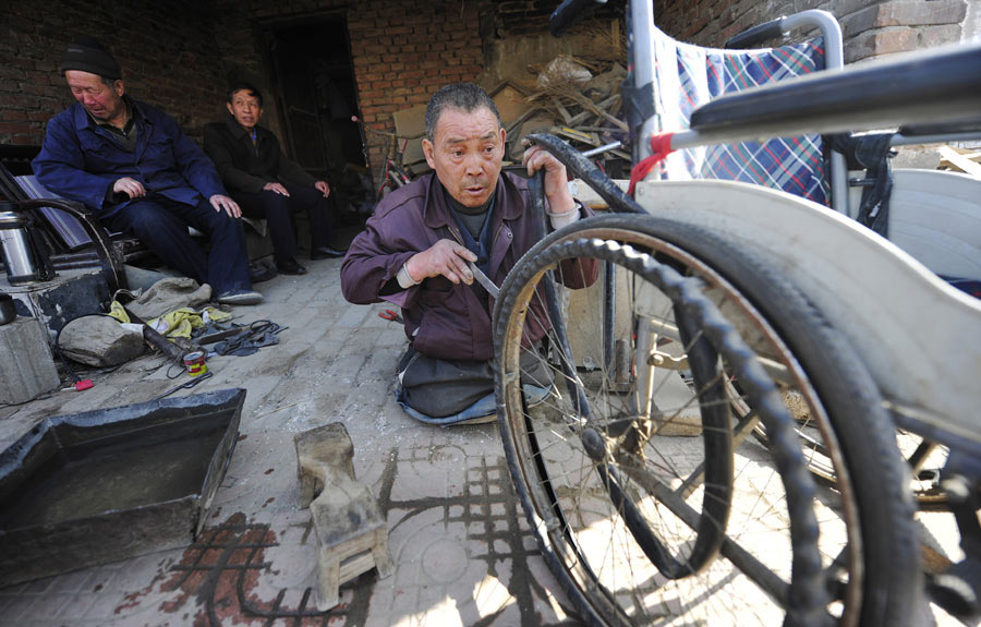 Lu Jianxin, quien perdió ambas extremidades en un incendio hace 30 años, arregla una silla de ruedas en Luoyang, provincia de Henan, el 16 de marzo, en un taller de reparación de bicicletas que ha dirigido desde hace más de dos décadas. [Fotografía por Huang Zhengwei/Asianewsphoto]