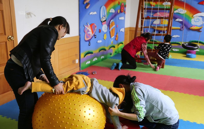 Una madre y una profesora ayudan a un niño a practicar un ejercicio en un centro de rehabilitación de Kunming, el 1 de abril, en vísperas del Día Mundial de Concienciación sobre el Autismo, el 2 de abril. Los "niños de las estrellas", como se conoce a las personas autistas en China, tiene un desarrollo del lenguaje lento, con dificultades en la comunicación y falta de atención.  