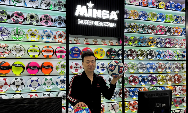 Chen Shaomei, gerente de Minsa Sports en el Mercado Internacional de Comercio de Yiwu, muestra dos balones de fútbol conmemorativos diseñados para la Copa Mundial de la FIFA 2026 que son los más populares entre los clientes extranjeros en Yiwu, provincia de Zhejiang, 15 de abril del 2026. (Foto: Cortesía)